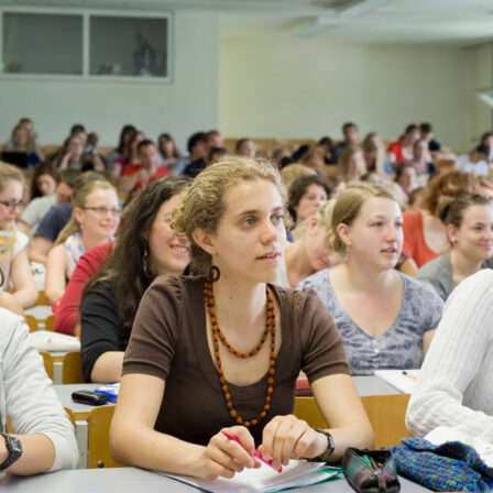 This is a picture of an auditorium full of students. They all look in the same direction. They seem to be listening intently. Some are taking notes.